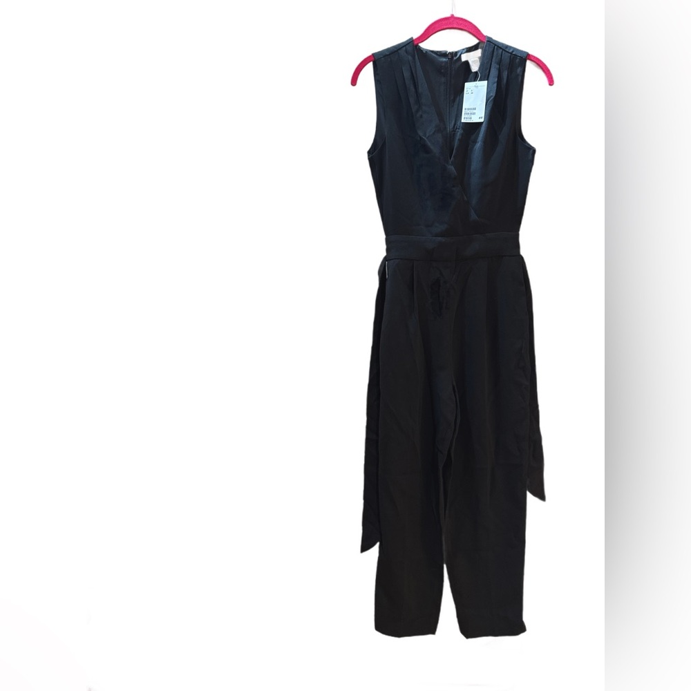 A sleeveless black jumpsuit with pleated shoulders and a belted waist